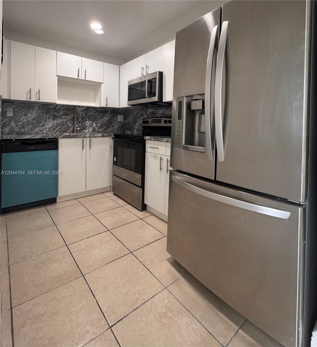 A kitchen features white cabinets, stainless steel appliances, a dark stone backsplash, and tiled floors — 1820 W 53rd St # 517, Hialeah FL 33012, HIALEAH, FL
