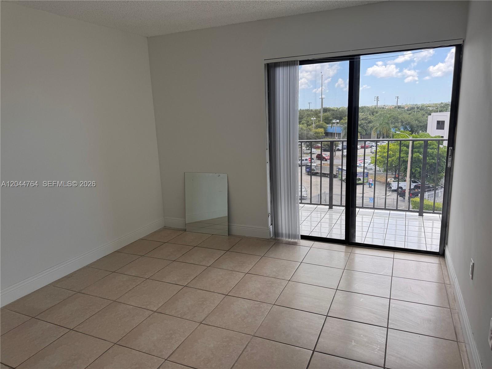 An empty room features beige tile flooring, white walls, and a sliding glass door to a balcony — 1820 W 53rd St # 517, Hialeah FL 33012, HIALEAH, FL
