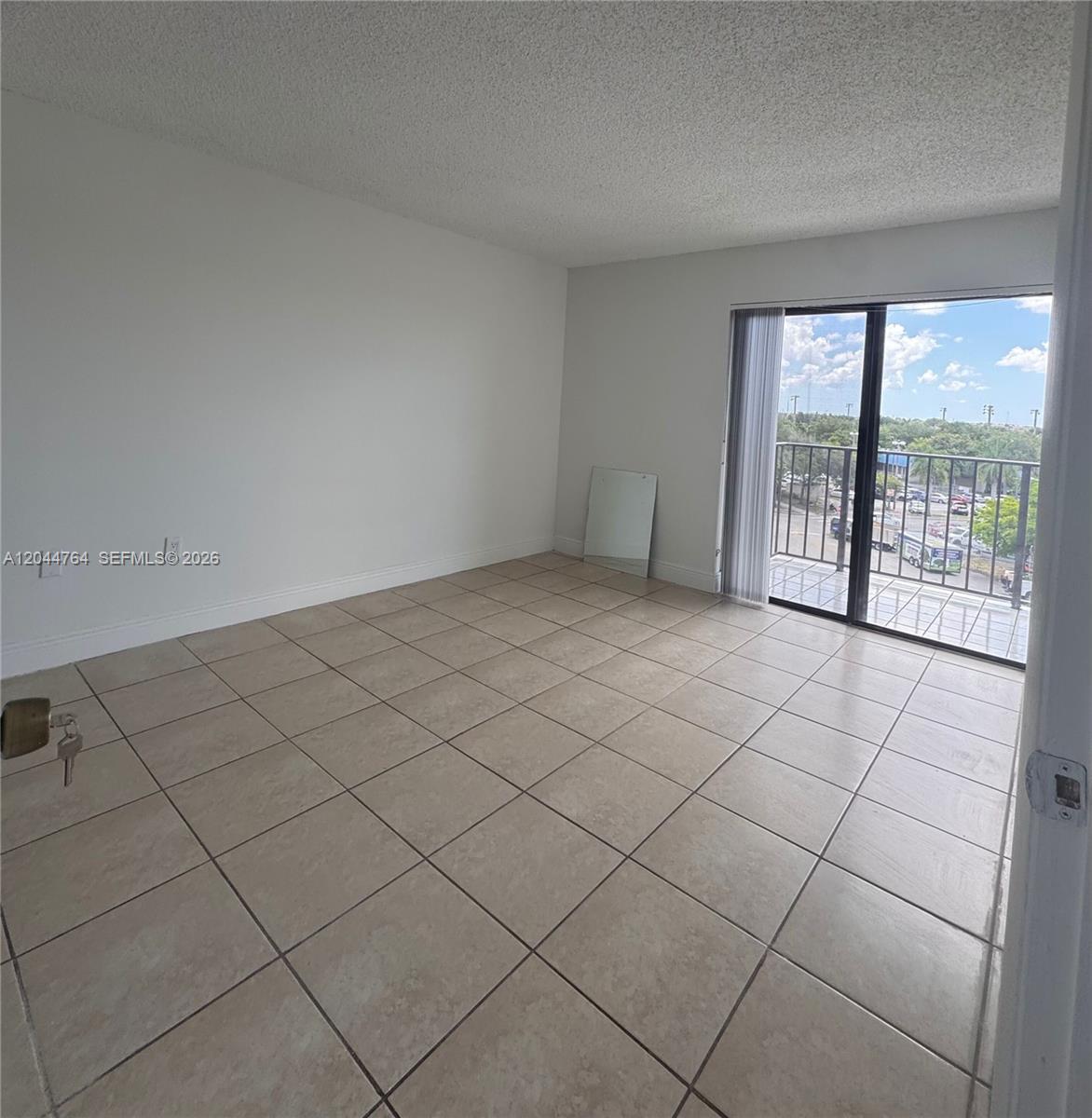 An empty room features beige tile flooring, white walls, and a sliding glass door to a balcony — 1820 W 53rd St # 517, Hialeah FL 33012, HIALEAH, FL