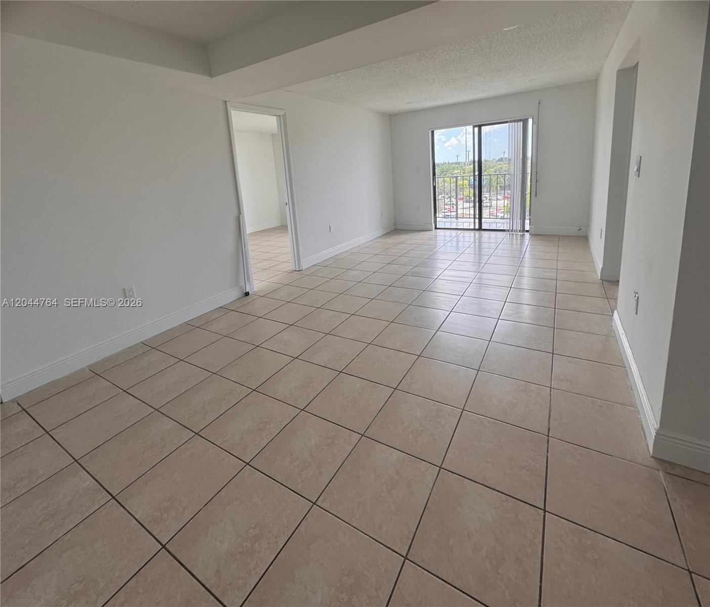 An empty room features beige tile flooring, white walls, and a sliding glass balcony door — 1820 W 53rd St # 517, Hialeah FL 33012, HIALEAH, FL