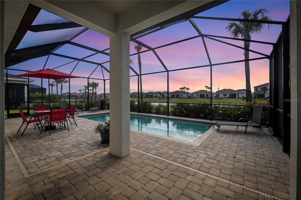 A screened-in patio features a swimming pool, paver flooring, and a view of a pond — 16941 SAGE TERRACE, PUNTA GORDA, FL