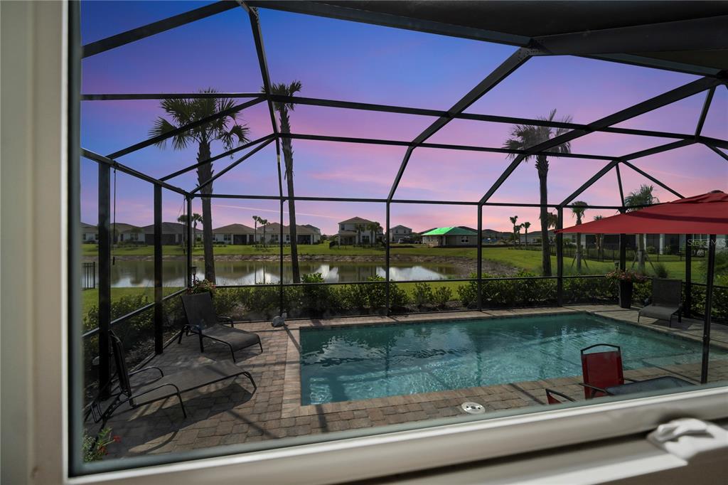A screened-in pool patio overlooks a pond and neighborhood houses at sunset — 16941 SAGE TERRACE, PUNTA GORDA, FL