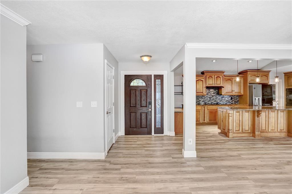 An entryway with light wood-look flooring leads to a dark wood front door and kitchen — 8404 BLACKSTONE COURT, TAMPA, FL