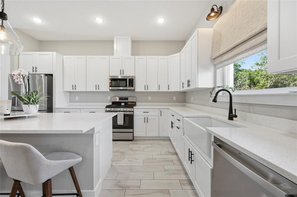 A modern kitchen features white cabinetry, quartz countertops, a farmhouse sink, and stainless steel appliances — 5777 SW 140TH AVENUE, OCALA, FL