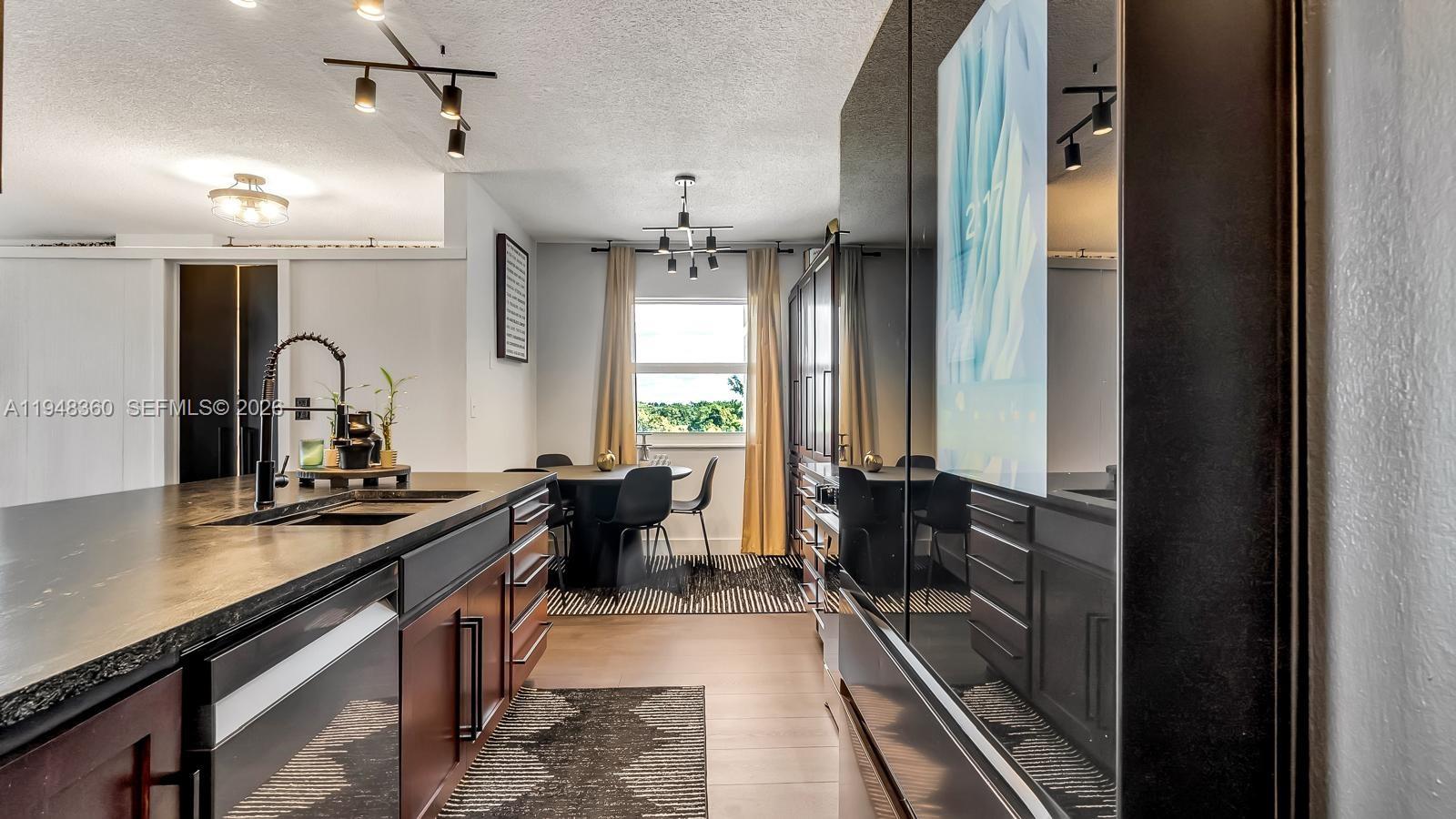 A modern kitchen features dark cabinetry, a black island countertop, and a dining area — 3800 Hillcrest Dr # 401, Hollywood FL 33021, HOLLYWOOD, FL
