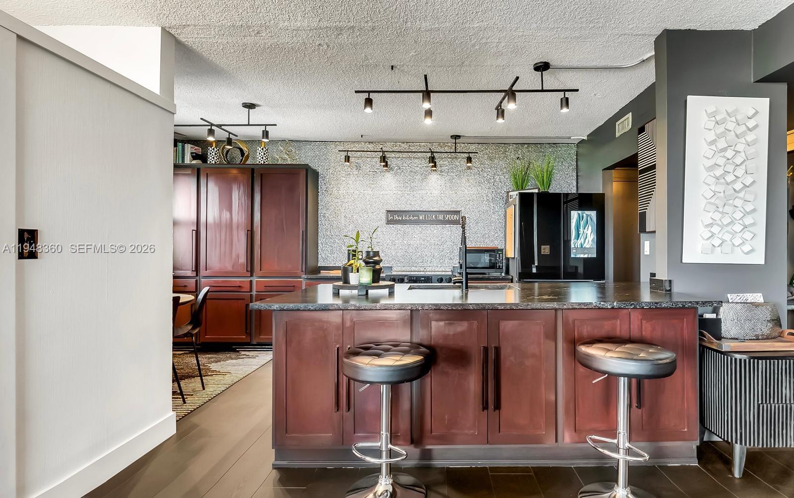A kitchen features dark wood cabinetry, a black island with bar stools, and track lighting — 3800 Hillcrest Dr # 401, Hollywood FL 33021, HOLLYWOOD, FL