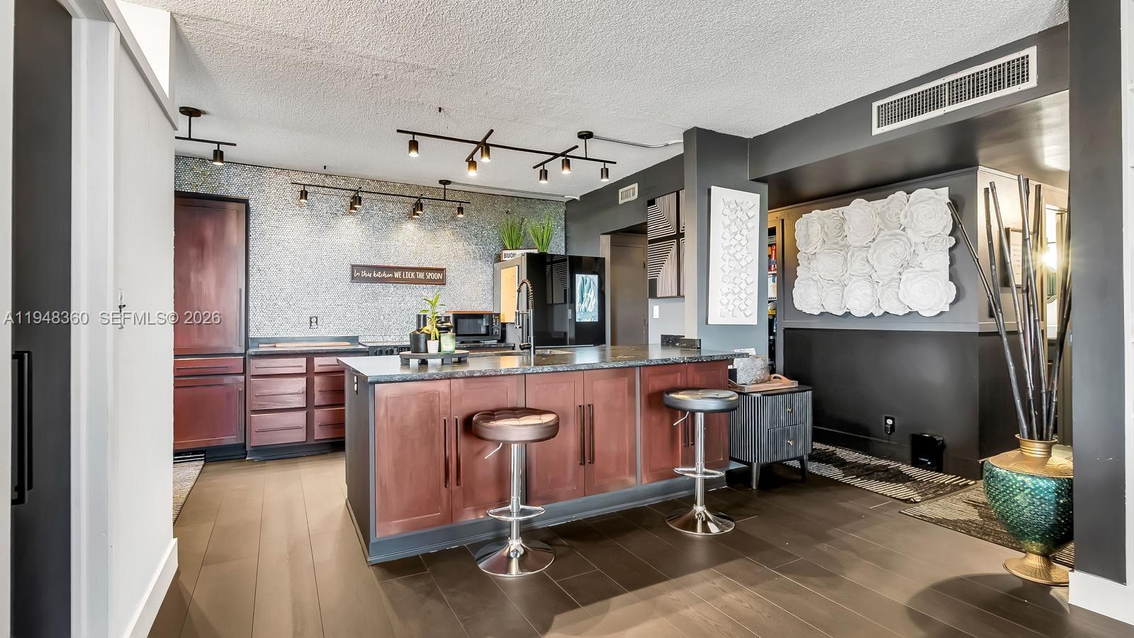 A kitchen features a dark wood island with bar stools, a mosaic backsplash, and track lighting — 3800 Hillcrest Dr # 401, Hollywood FL 33021, HOLLYWOOD, FL