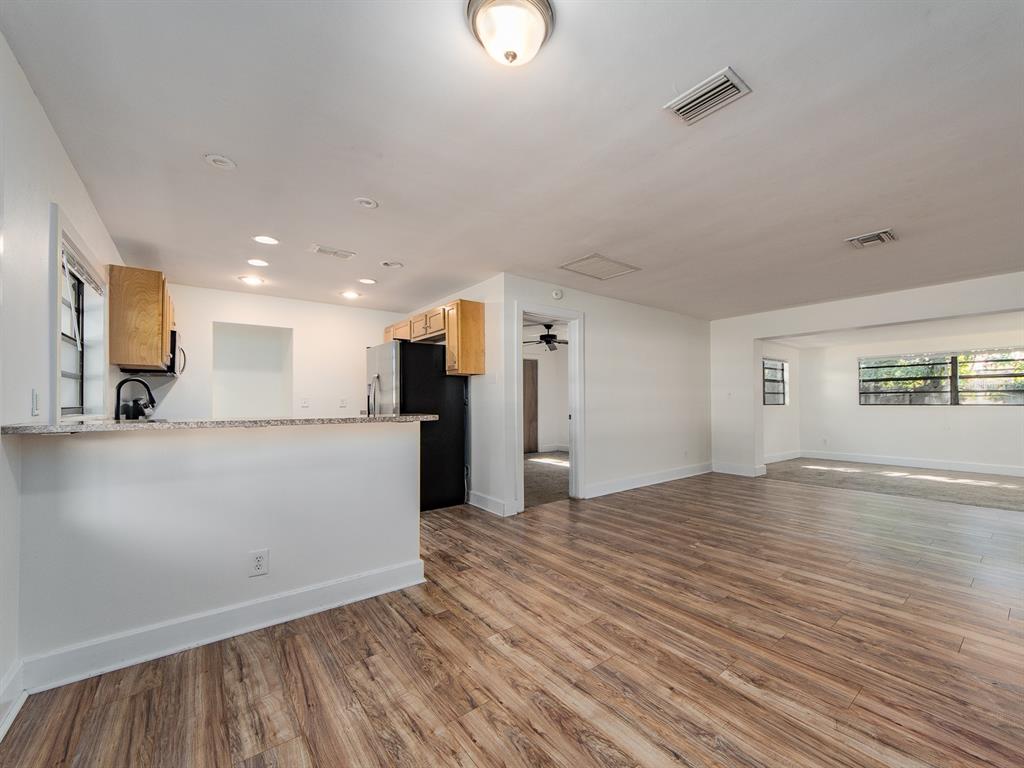 An open-concept kitchen and living area featuring wood-look flooring, white walls, and a breakfast bar — 2242 INDIAN AVENUE S, LARGO, FL