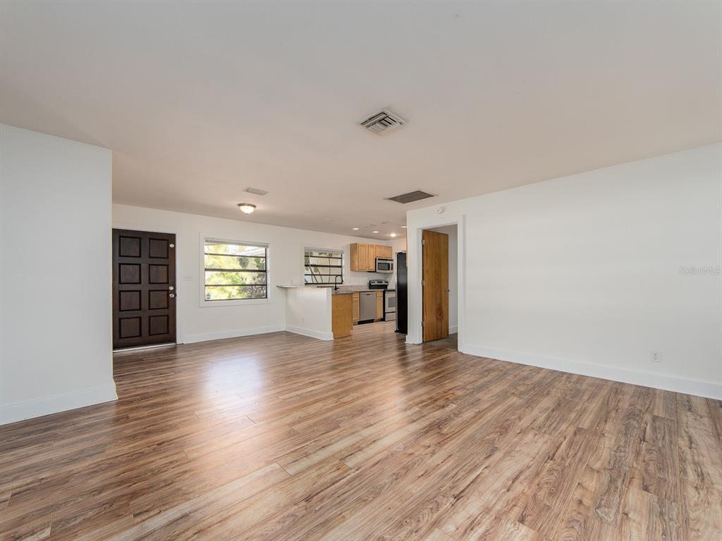An open-concept living area features wood-look flooring, white walls, and a kitchen with light cabinetry — 2242 INDIAN AVENUE S, LARGO, FL