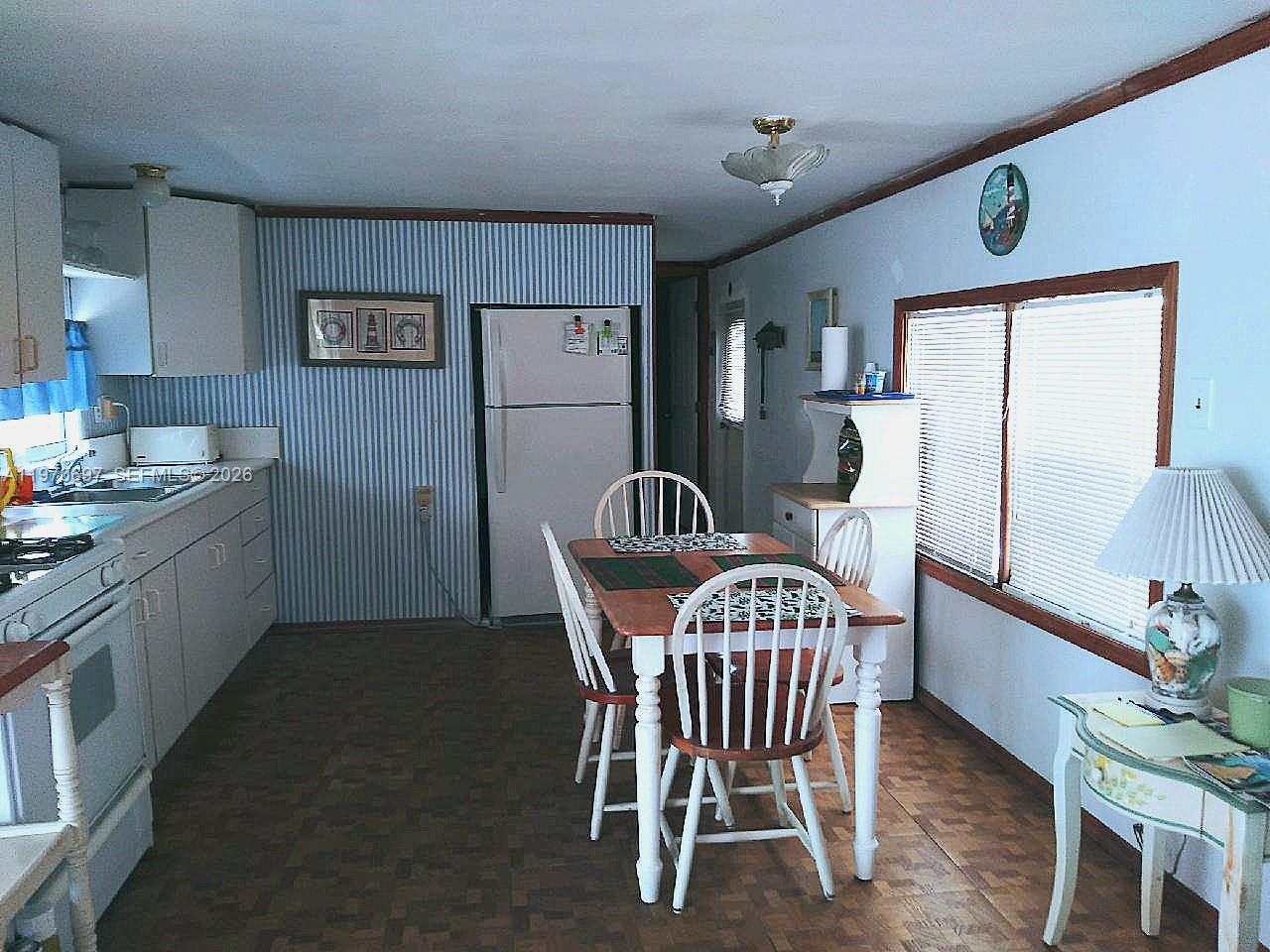 A kitchen and dining area with striped wallpaper, white cabinets, and a wooden dining table — 261 Burgundy Dr, Tavernier FL 33070, TAVERNIER, FL