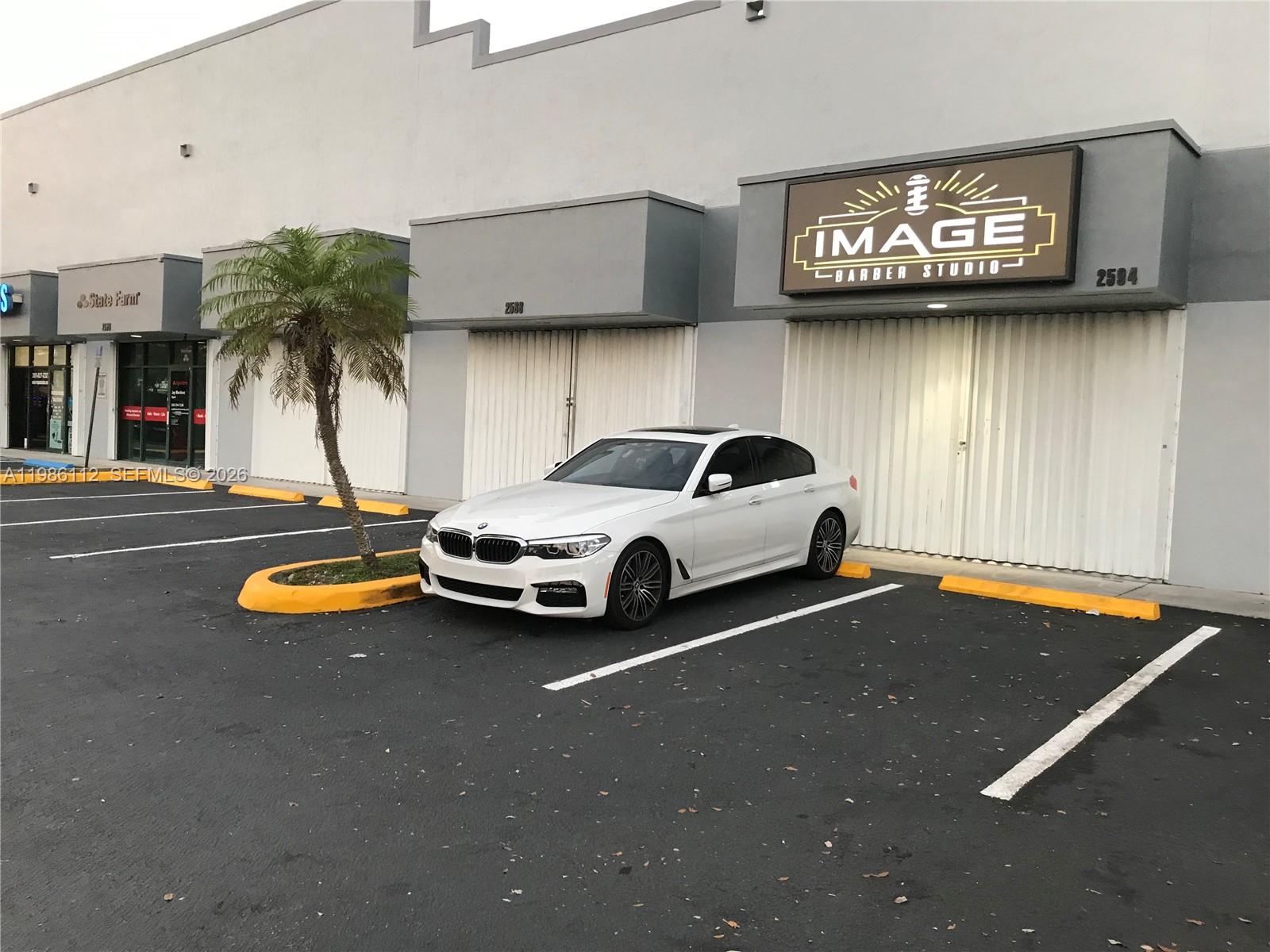 A white BMW sedan is parked in front of a commercial building with a barber shop — 8353 W 26th Ave # B, Hialeah FL 33016, HIALEAH, FL