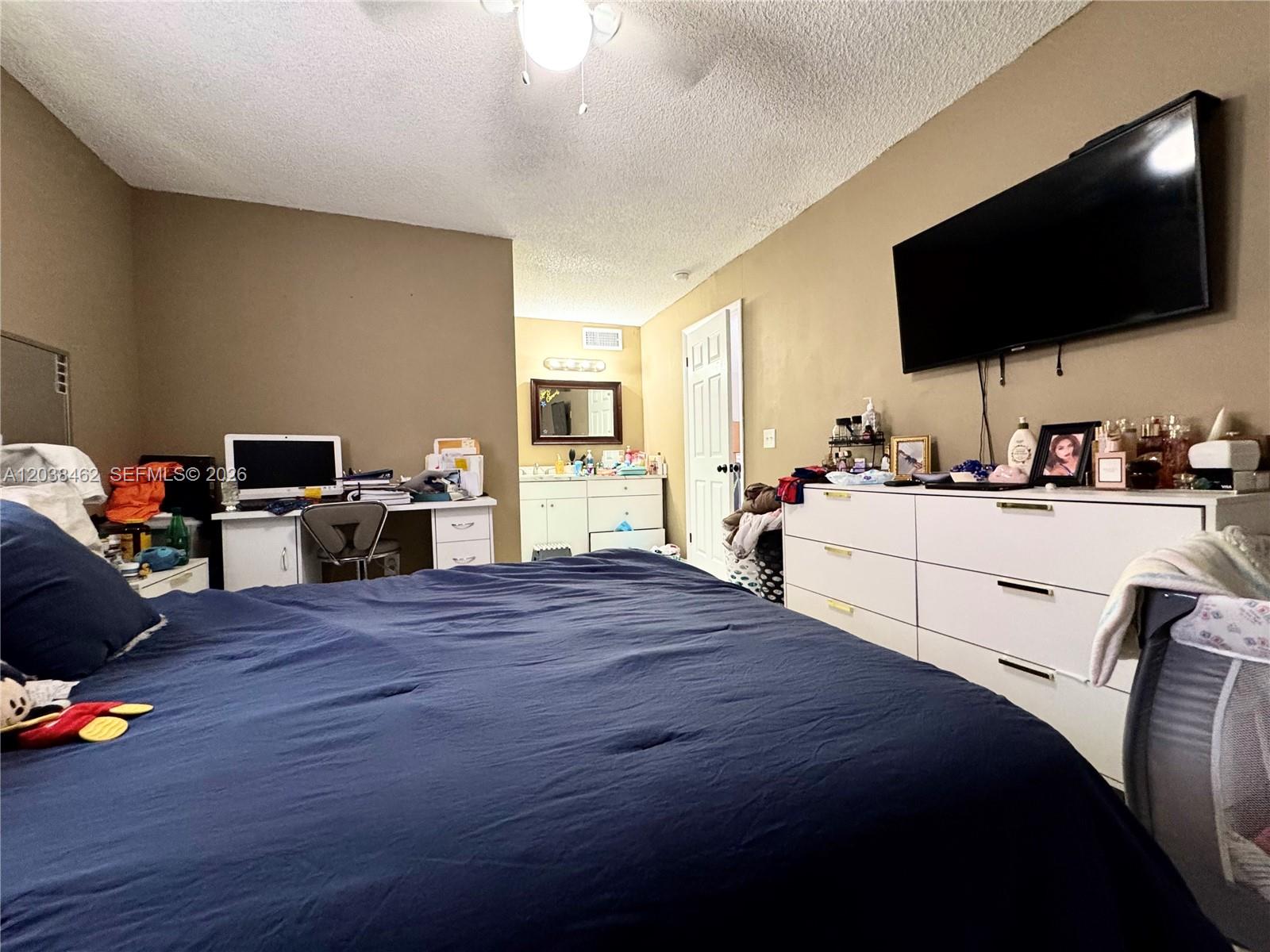 A bedroom features a dark blue bed, a white desk, a white dresser, and a television — 19729 SW 114th Ave # 250, Miami FL 33157, MIAMI, FL