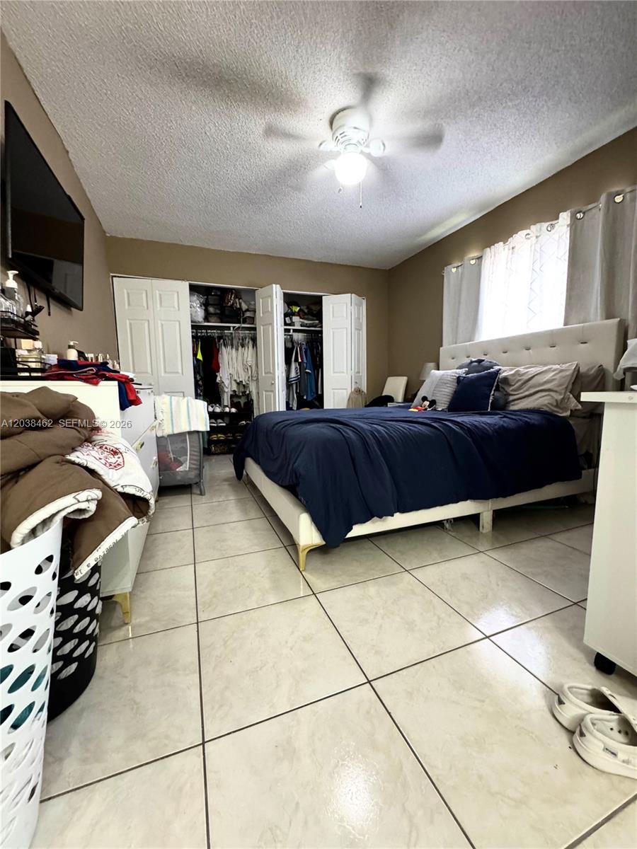 A bedroom features a bed with a navy comforter, tiled floors, and open closet doors — 19729 SW 114th Ave # 250, Miami FL 33157, MIAMI, FL