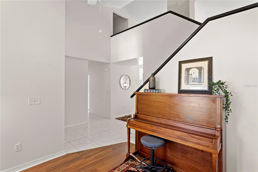 A wooden upright piano sits against a wall near a staircase in a foyer — 7210 HAMMET ROAD, TAMPA, FL
