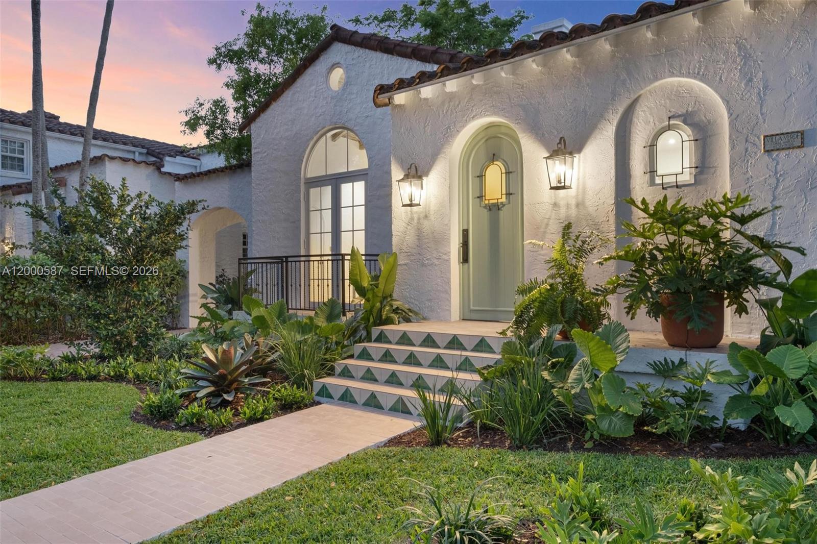 A white stucco house with a tiled roof features a green arched door and steps — 909 Roderigo Ave, Coral Gables FL 33134, CORAL GABLES, FL