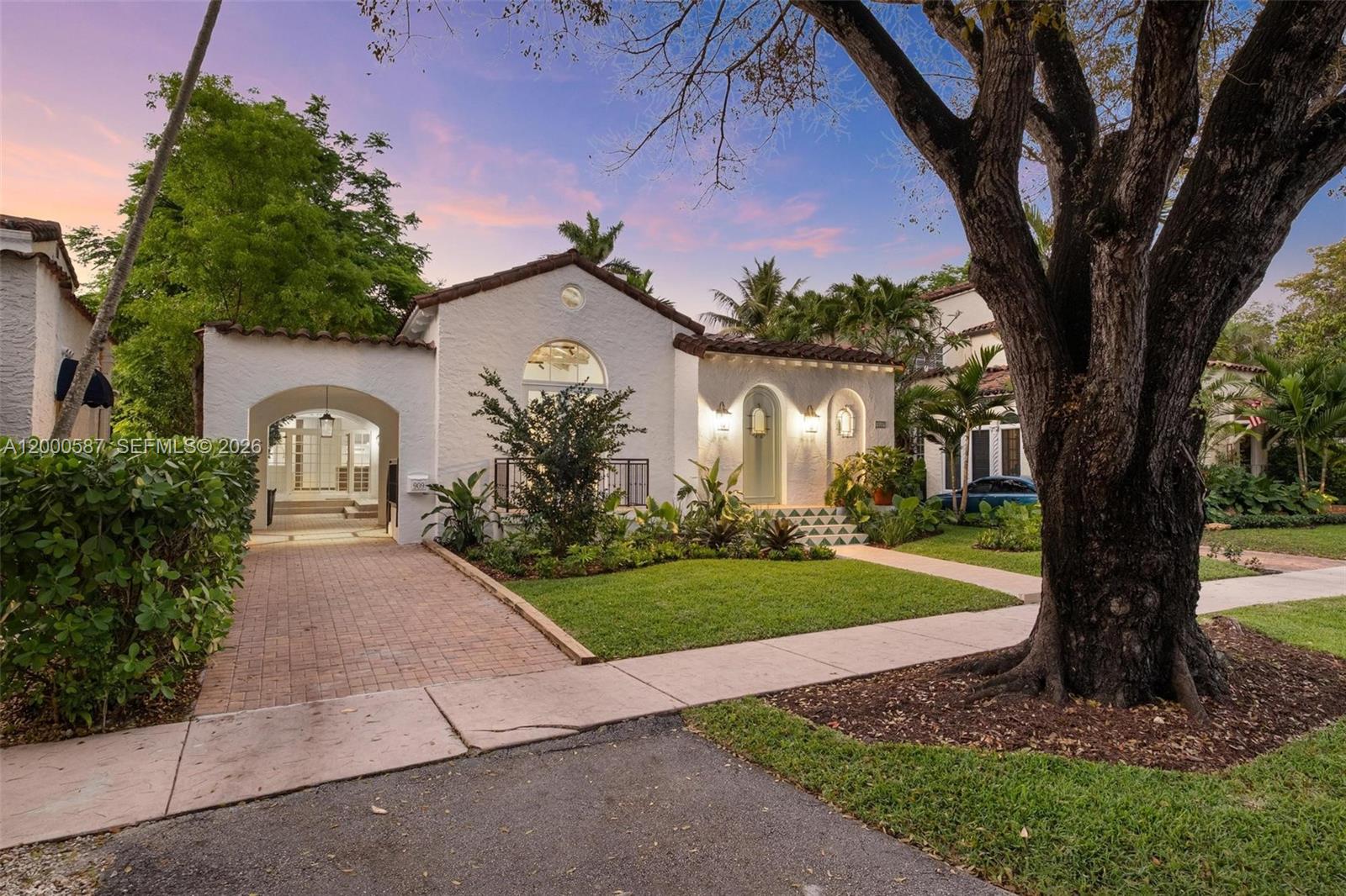 A white stucco house with a tiled roof features an arched entryway and brick driveway — 909 Roderigo Ave, Coral Gables FL 33134, CORAL GABLES, FL
