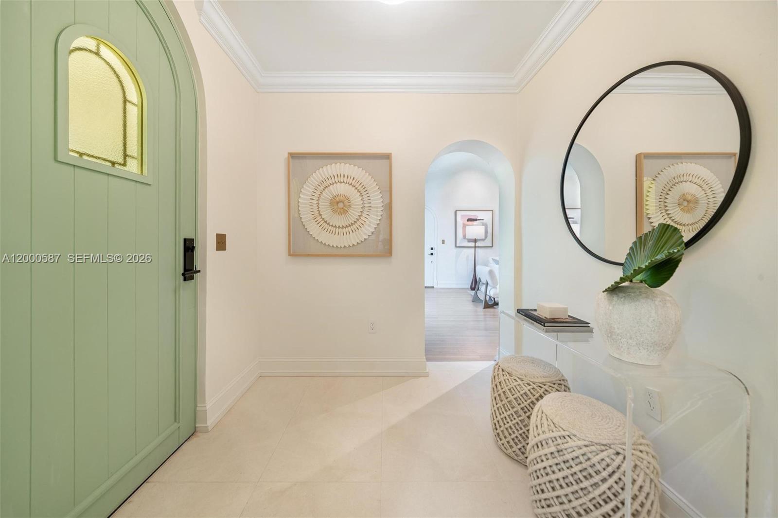 A light-filled entryway features a sage green arched door, white tile floors, and wall art — 909 Roderigo Ave, Coral Gables FL 33134, CORAL GABLES, FL