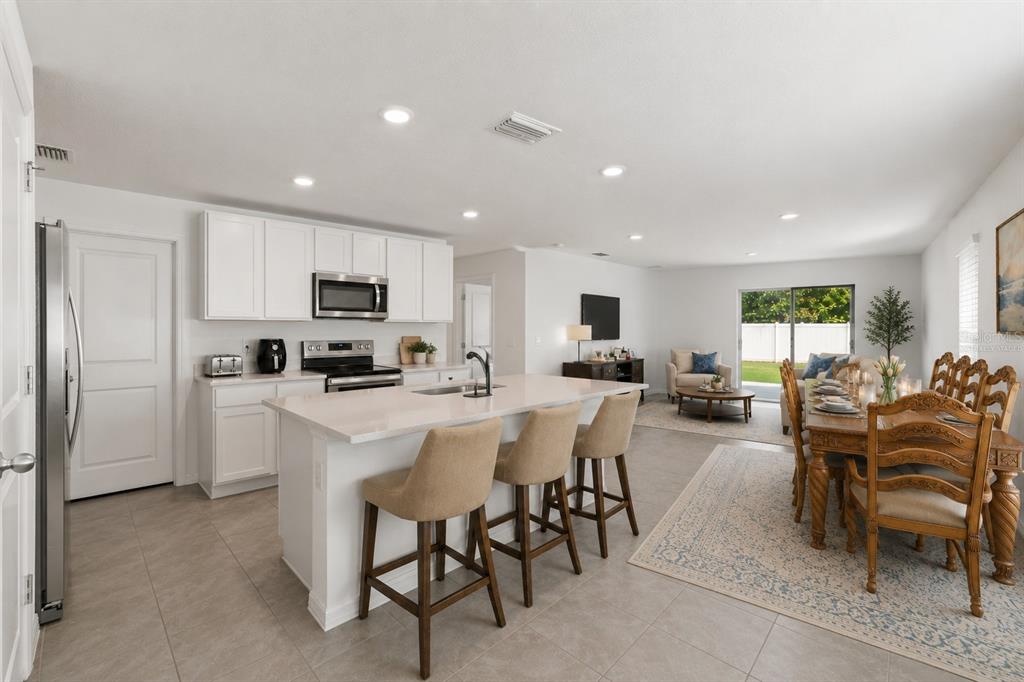 An open-concept kitchen with white cabinets, a quartz island, and an adjacent dining area — 37445 SHARKS EYE LANE, ZEPHYRHILLS, FL