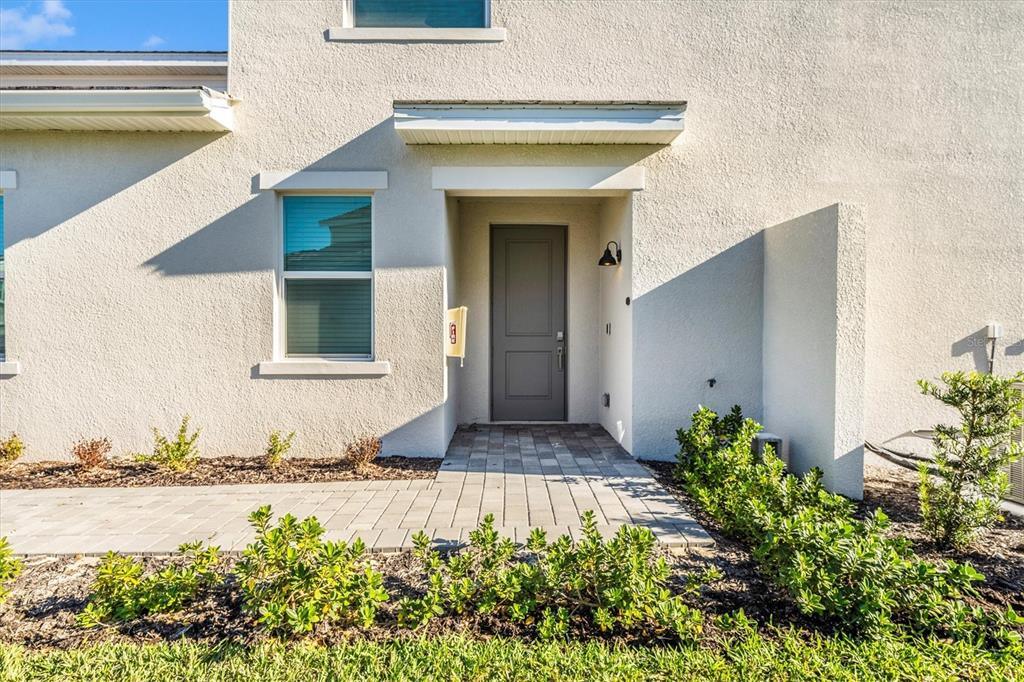 The exterior of a beige stucco house features a gray front door and paved walkway — 17700 BORACAY COURT UNIT 102, VENICE, FL