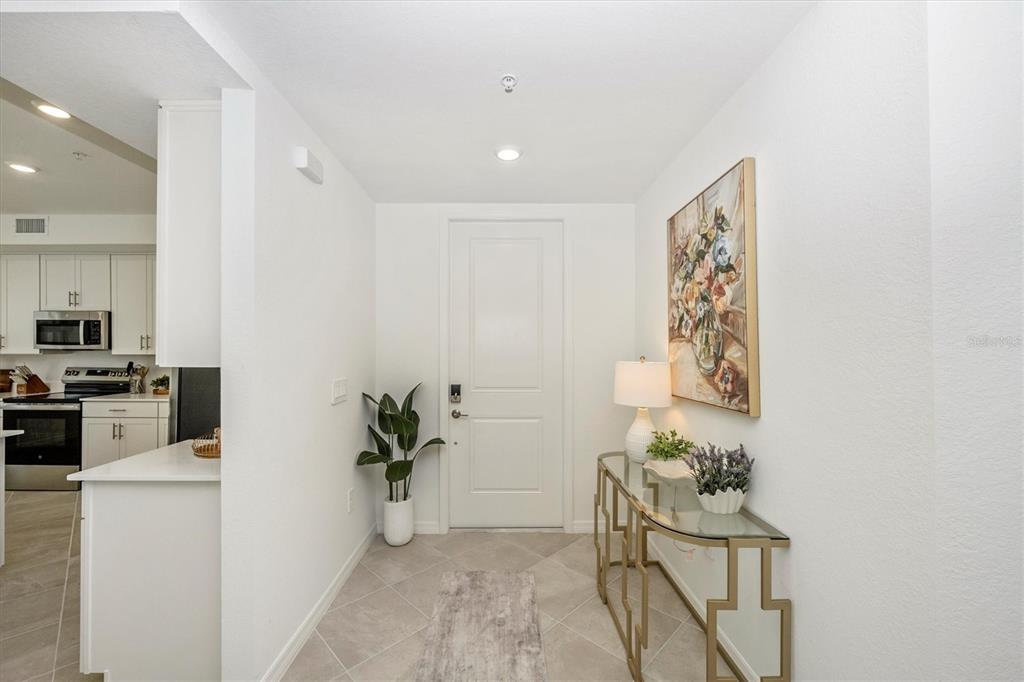 An entryway features a white door, a glass console table, and a view into the kitchen — 17700 BORACAY COURT UNIT 102, VENICE, FL