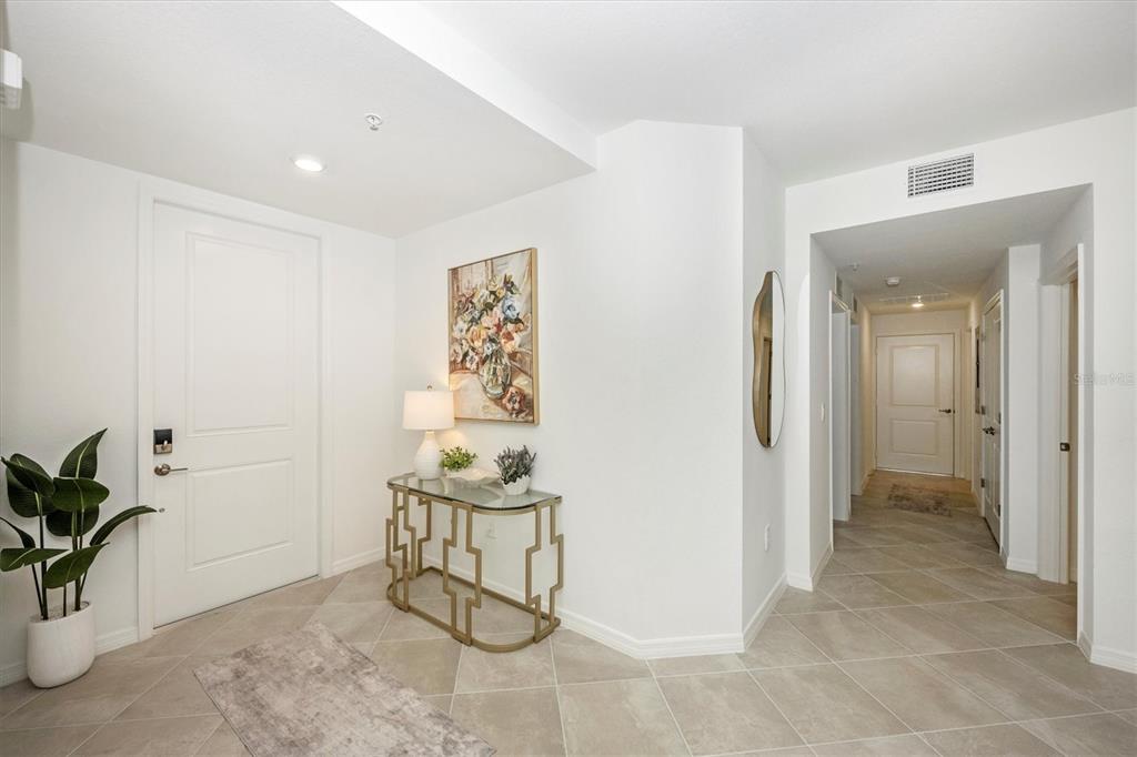 A bright entryway features tile flooring, a gold console table, and a white front door — 17700 BORACAY COURT UNIT 102, VENICE, FL