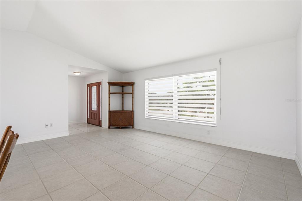 A bright, empty room features light-colored tile flooring, white walls, and a large window — 15184 ALDAMA CIRCLE, PORT CHARLOTTE, FL