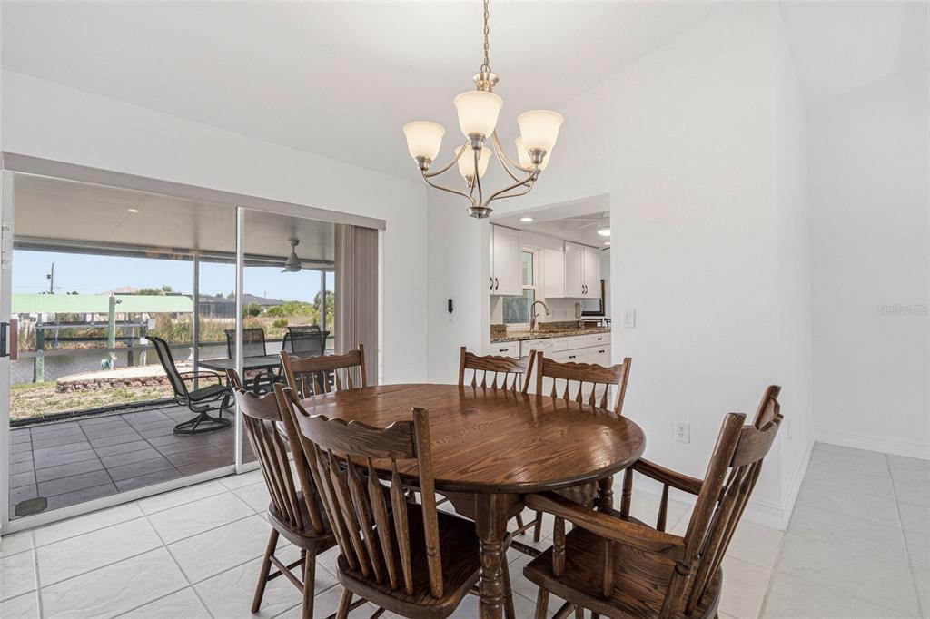 A dining area with a wooden table and chairs, a chandelier, and a sliding glass door — 15184 ALDAMA CIRCLE, PORT CHARLOTTE, FL
