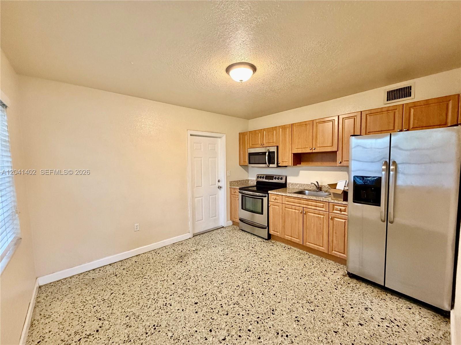 A kitchen features light wood cabinets, stainless steel appliances, and speckled terrazzo flooring — 911 NW 22nd Pl # 0, Miami FL 33125, MIAMI, FL