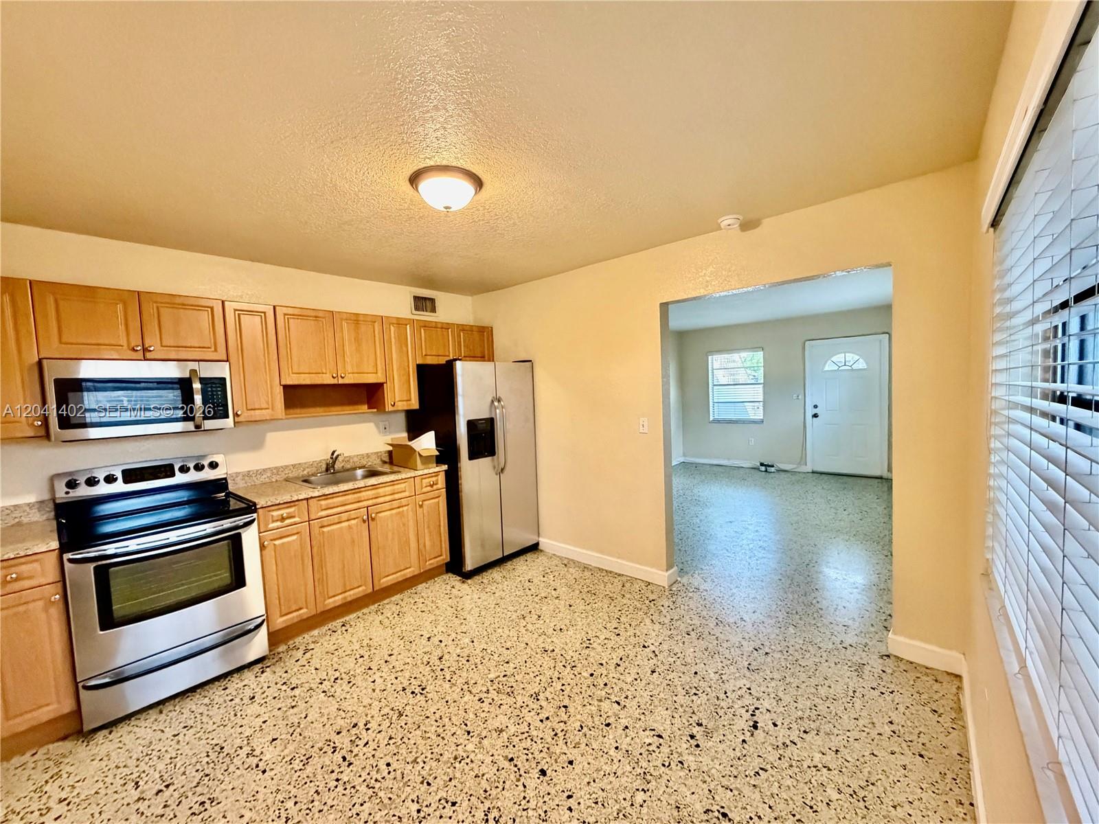 A kitchen with light wood cabinets, stainless steel appliances, and speckled flooring leads to a living area — 911 NW 22nd Pl # 0, Miami FL 33125, MIAMI, FL