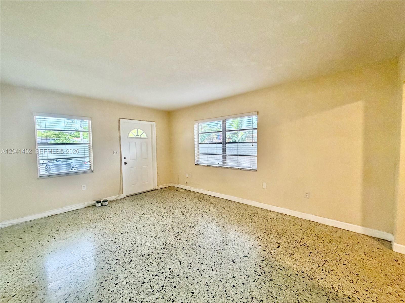 An empty room features light-colored walls, two windows with blinds, and speckled terrazzo flooring — 911 NW 22nd Pl # 0, Miami FL 33125, MIAMI, FL