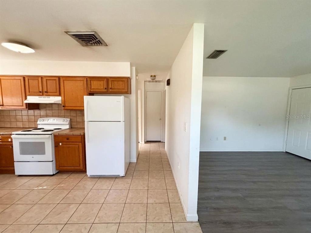 A kitchen with wood cabinets and tile floors opens into a living area with flooring — 1240 JOSEPHINE STREET, LAKELAND, FL