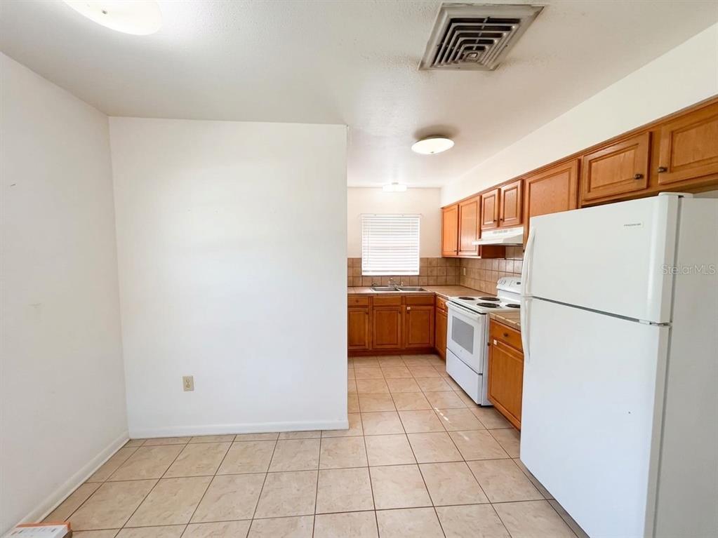 A kitchen features wood cabinets, white appliances, and light-colored tile flooring — 1240 JOSEPHINE STREET, LAKELAND, FL