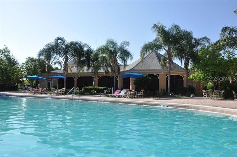 A swimming pool sits in front of a clubhouse building with palm trees and umbrellas — 602 NEW PROVIDENCE PROMENADE UNIT 17602, DAVENPORT, FL