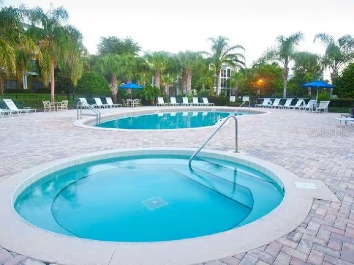 A circular hot tub sits in the foreground of a paved pool deck with lounge chairs — 602 NEW PROVIDENCE PROMENADE UNIT 17602, DAVENPORT, FL