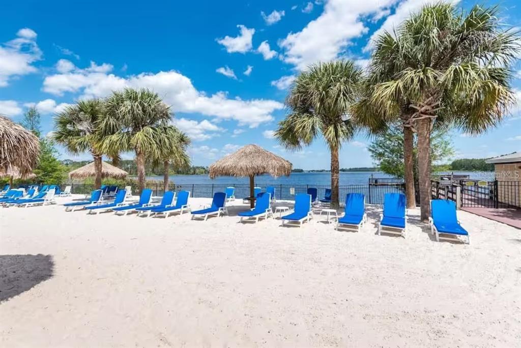 A sandy beach area features rows of blue lounge chairs under palm trees by water — 602 NEW PROVIDENCE PROMENADE UNIT 17602, DAVENPORT, FL