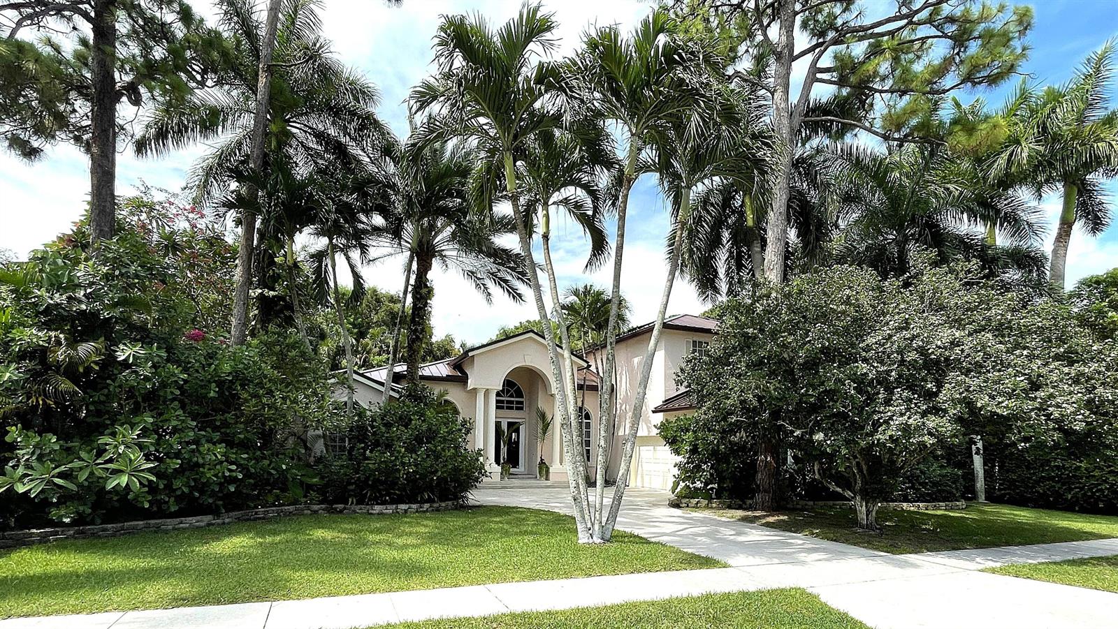 A single-story house with a prominent arched entryway is surrounded by lush palm trees — 4740 Glenn Pine Lane, Boynton Beach FL 33436, BOYNTON BEACH, FL