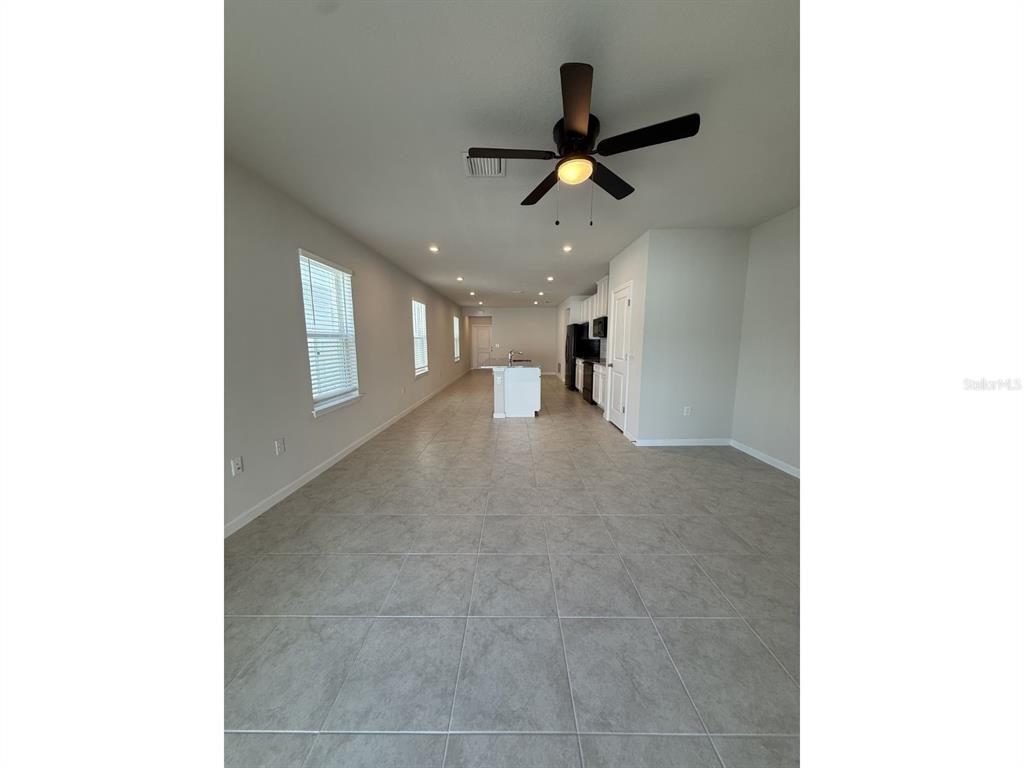 An open-concept room features light-colored tile flooring, a ceiling fan, and a kitchen island — 11921 BRISTOL BRIDGE ROAD, SPRING HILL, FL