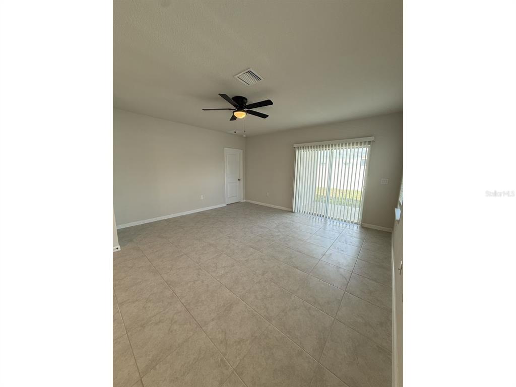 An empty room features light-colored tile flooring, a ceiling fan, and sliding glass doors — 11921 BRISTOL BRIDGE ROAD, SPRING HILL, FL