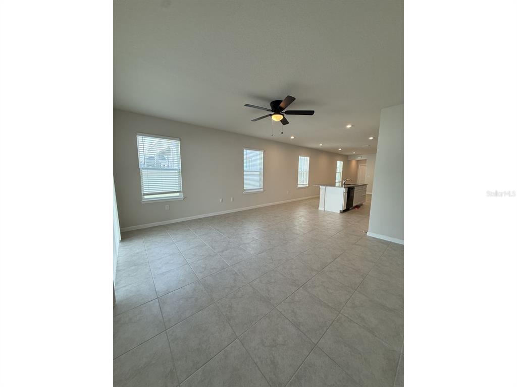 An open-concept living area features light tile flooring, a ceiling fan, and a kitchen island — 11921 BRISTOL BRIDGE ROAD, SPRING HILL, FL
