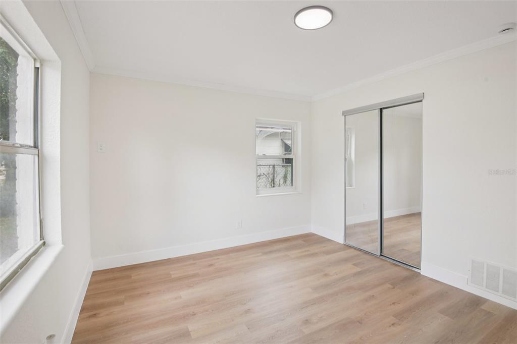 A bedroom with white walls, light wood-look flooring, a window, and mirrored sliding closet doors — 3468 9TH AVENUE N, ST PETERSBURG, FL