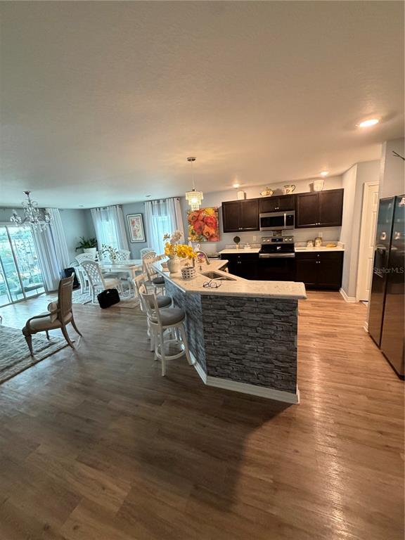 An open-concept kitchen features dark cabinetry, a stone-veneer breakfast bar, and light wood flooring — 3024 FIELDWOOD CIRCLE, ST CLOUD, FL