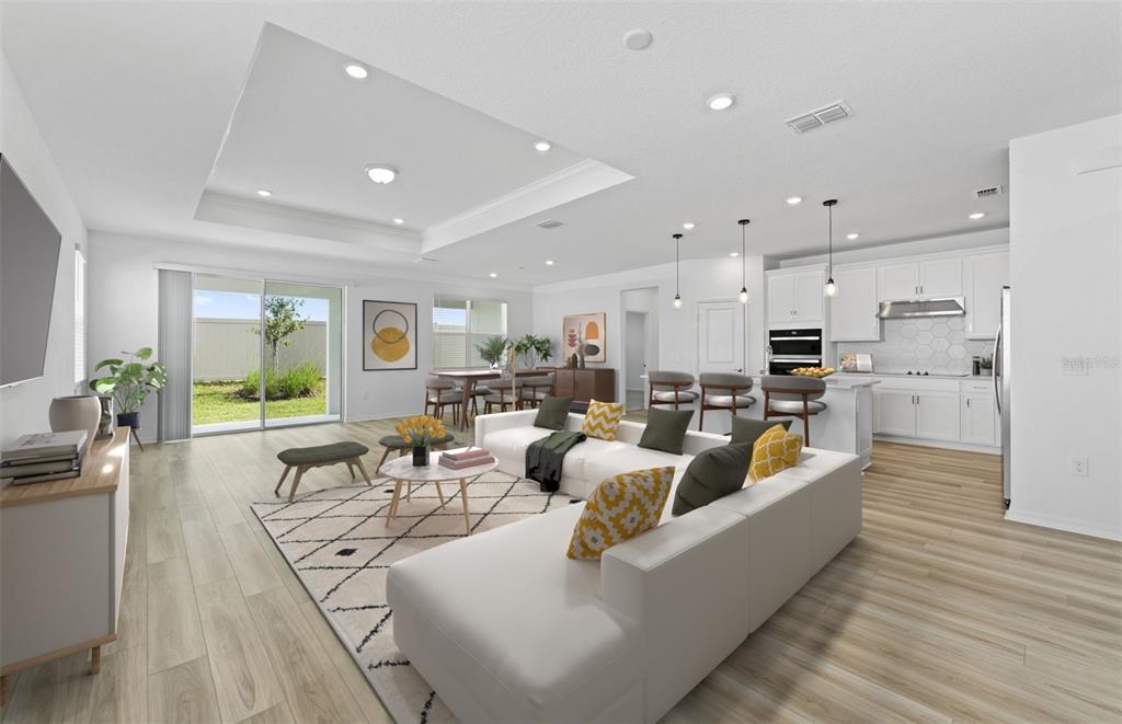 A bright open-concept living room and kitchen featuring white cabinetry, wood-look flooring, and sliding doors — 16816 HARMONY RIVER LANE, PARRISH, FL