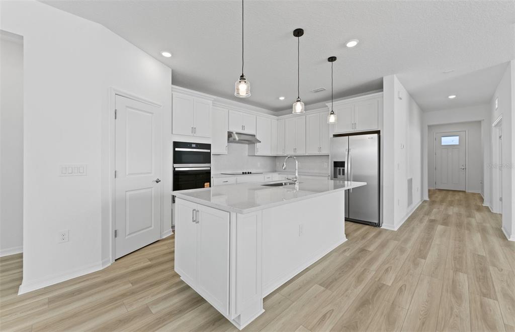 A modern kitchen features white cabinetry, a central island, stainless steel appliances, and light flooring — 16816 HARMONY RIVER LANE, PARRISH, FL