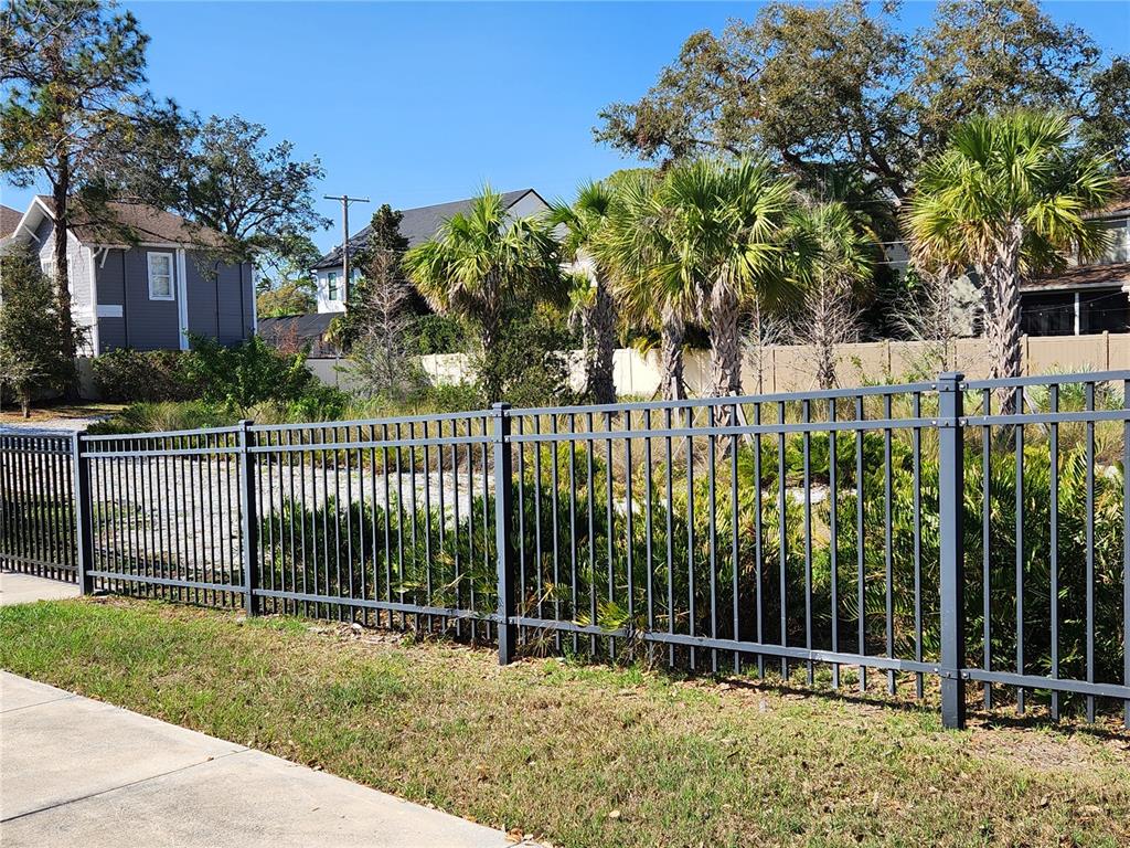 A metal fence borders a grassy lot with palm trees and nearby houses — 4409 W EL PRADO BOULEVARD, TAMPA, FL
