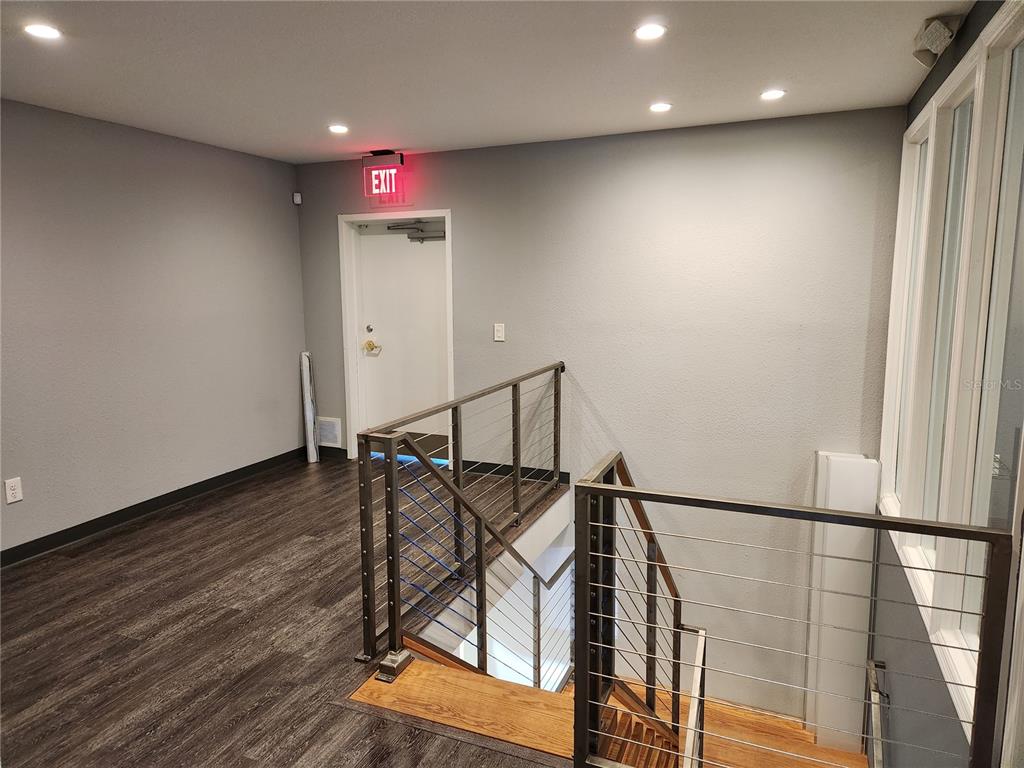 A landing with dark wood flooring, a staircase with metal railings, and an exit door — 4409 W EL PRADO BOULEVARD, TAMPA, FL