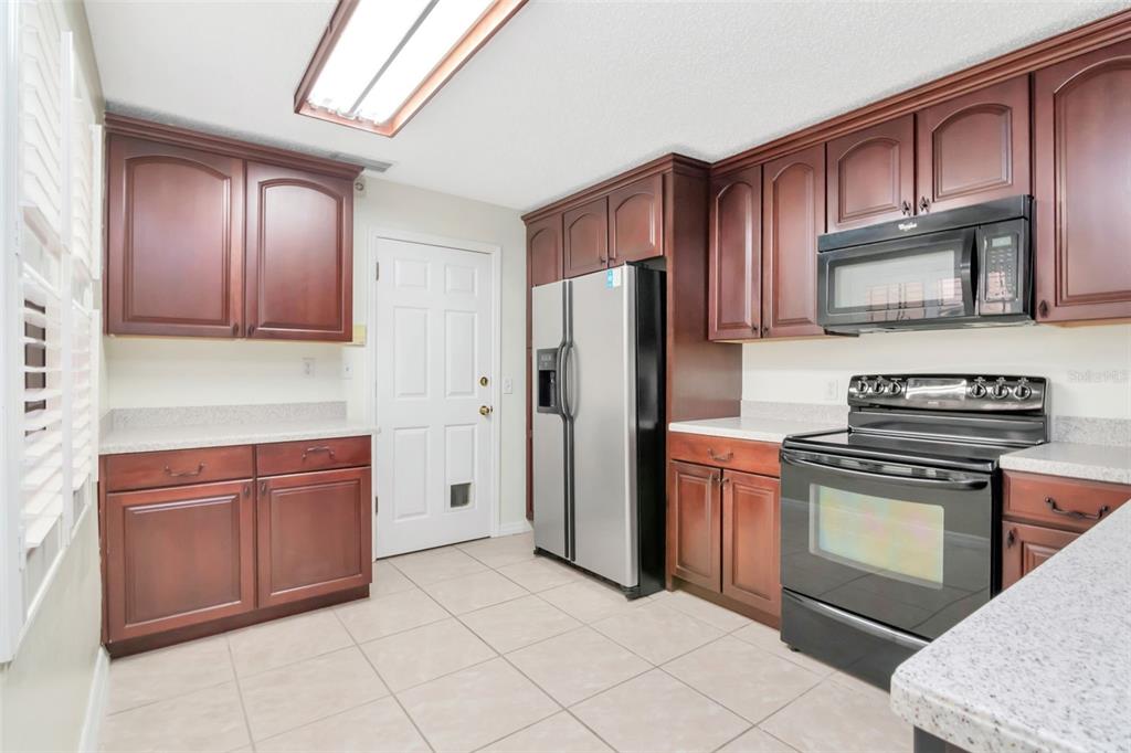 A kitchen with dark wood cabinets, stainless steel appliances, and light-colored tile flooring — 10417 SAINT TROPEZ PLACE UNIT 103, TAMPA, FL