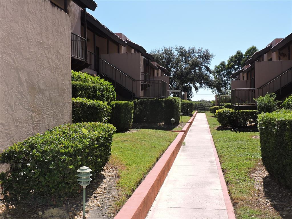 A concrete walkway leads between two rows of multi-story apartment buildings with landscaped hedges — 133 LA CASA UNIT 133, LAKE WALES, FL
