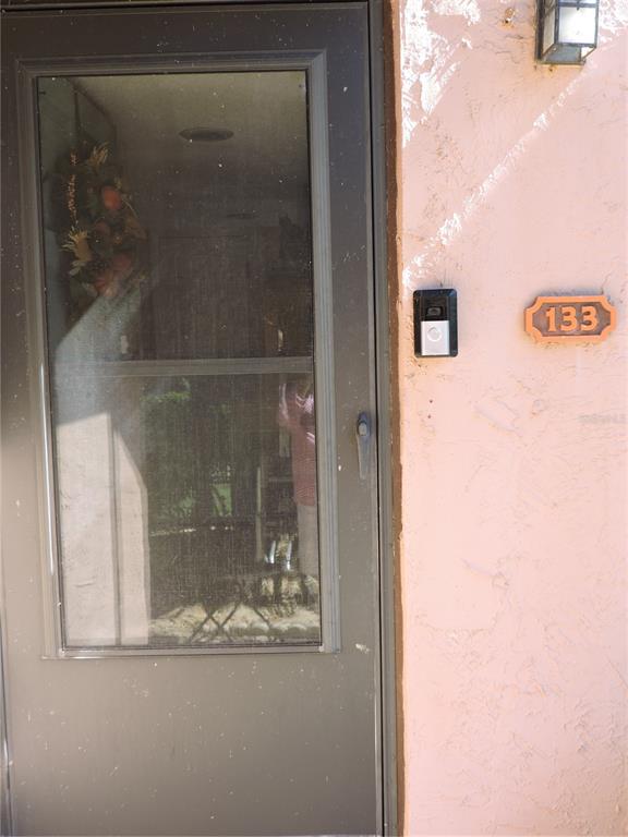 A brown storm door with a glass panel is mounted on a pink stucco wall — 133 LA CASA UNIT 133, LAKE WALES, FL