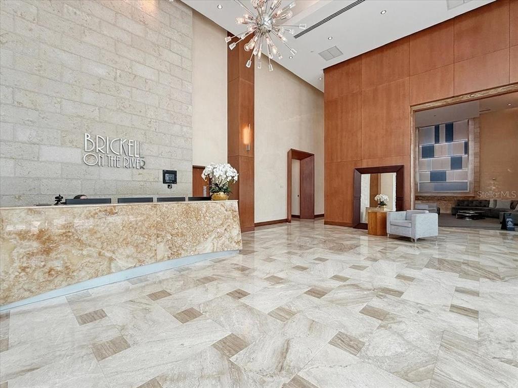 A modern building lobby features a stone reception desk, marble floors, and a large chandelier — 31 SE 5TH STREET UNIT 203, MIAMI, FL