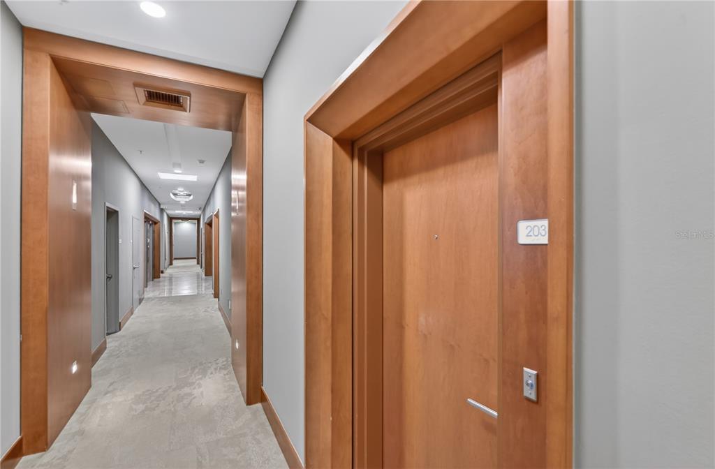 A long hallway with light-colored carpet, grey walls, and wood-trimmed doorways leads to unit 203 — 31 SE 5TH STREET UNIT 203, MIAMI, FL